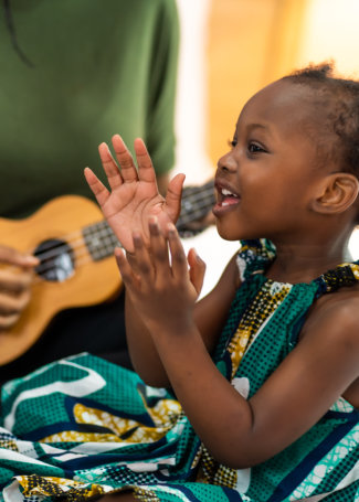 Happy Mom with her daughter playing guitar and singing together at home