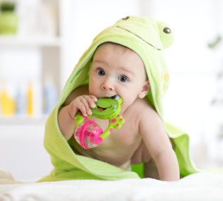 Baby boy with green towel after the bath biting toy